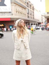 A lady wears a white tweed jacket.